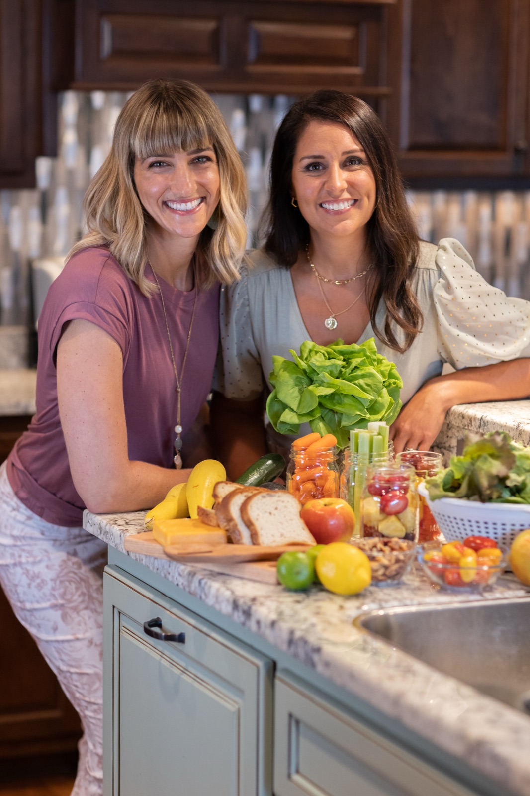 The two Gut Girls founders leaning on a kitchen counter filled with fresh produce