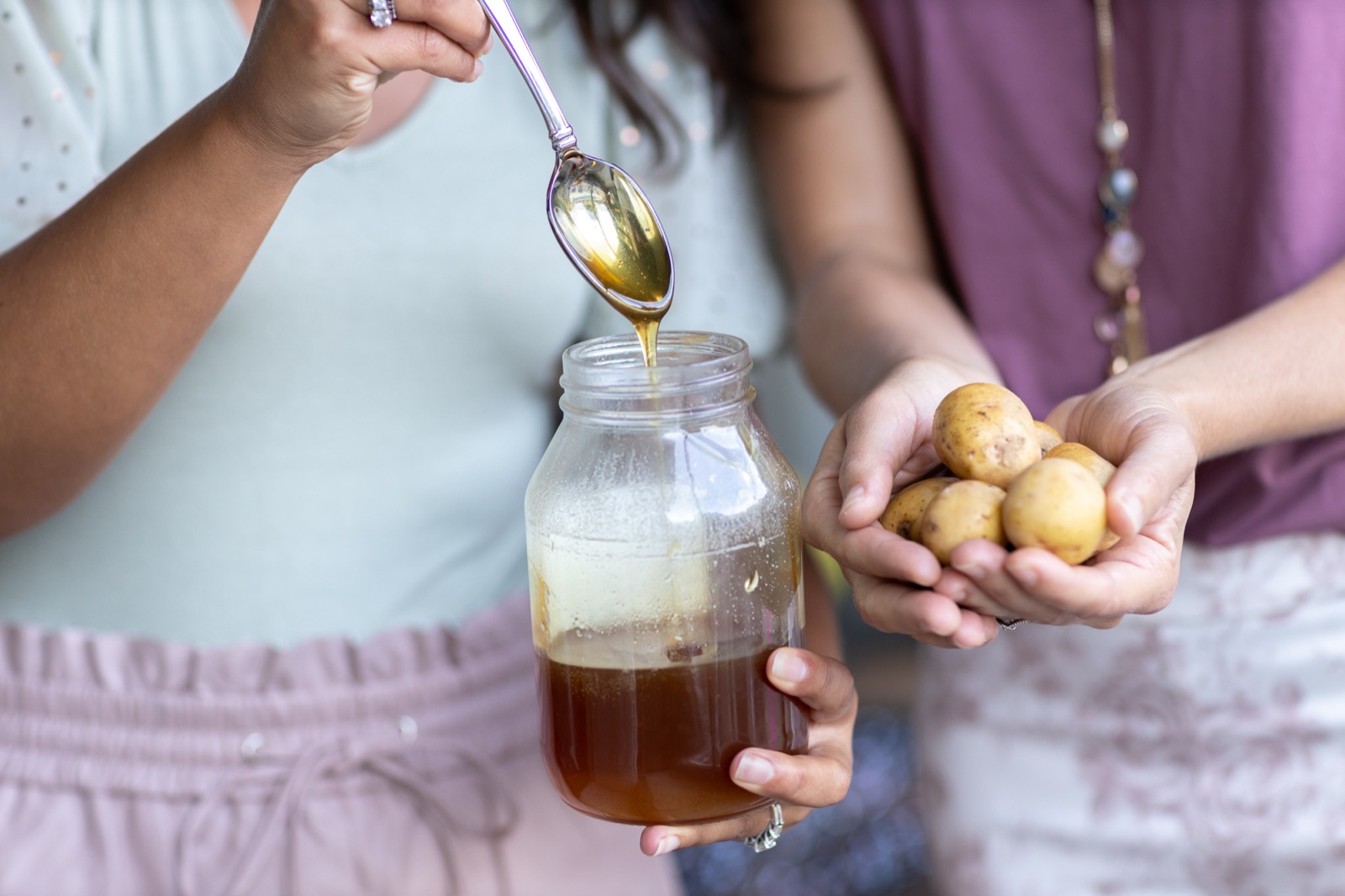 A spoonful of honey drizzling over a jar of bone broth next to a handful of small potatoes